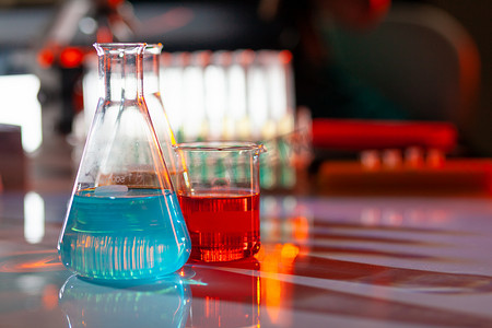 照明的实验室烧瓶里装满了五颜六色的化学溶液，桌子上有阴影。