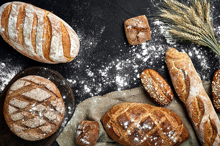 黑板白色背景摄影照片_法式长棍面包、烤面包、面粉和小麦穗组合物的顶视图，深色背景上撒有小麦粉