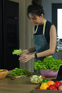 亚洲女人站在厨房的桌子前准备健康的素食沙拉。