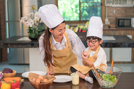 搞笑动图gif摄影照片_快乐美丽的亚洲女人和戴眼镜的可爱小男孩准备在家里的厨房做饭，搞笑。