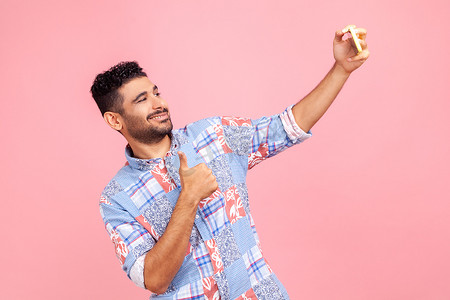 开朗英俊、留着胡子的男子穿着蓝色衬衫，竖起大拇指，做出赞同的手势，微笑着进行视频通话或在手机上流媒体。