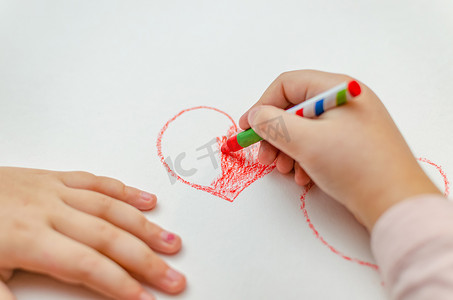 红笔画背景摄影照片_一个小女孩正在用红色粉笔画一颗心-有选择性聚焦的高角度图像。