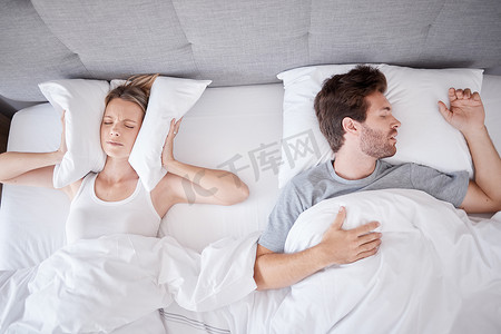 噪声摄影照片_睡觉、打鼾和妻子在耳朵上放枕头，以阻止有睡眠问题的丈夫在床上发出的噪音。