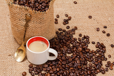 咖啡豆跌落摄影照片_一杯咖啡和烘焙过的咖啡豆装在帆布袋里。