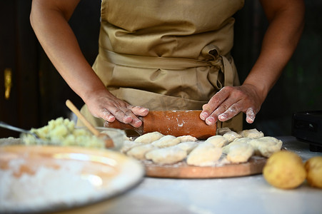 身着米色围裙的特写女厨师家庭主妇，用擀面杖擀出饺子面团，制作自制的瓦雷尼基