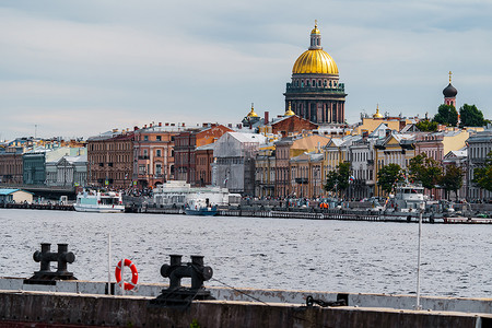 金色2022摄影照片_俄罗斯，圣彼得堡，2022年7月31日：阴天时，圣以撒大教堂巨大的金色圆顶穿过圣彼得堡涅瓦河堤上房屋的屋顶