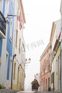 葡萄牙小镇的街道上有色彩缤纷的房屋、一条铺好的道路和一对夫妇沿着它散步