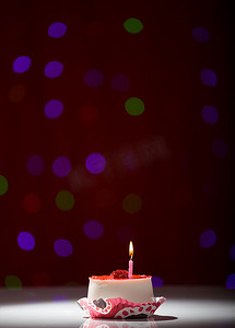 蜡烛模糊背景摄影照片_红色模糊背景上用蜡烛拍摄的生日快乐蛋糕
