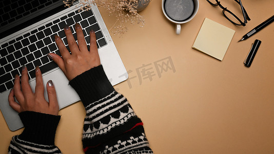 穿着温暖毛衣的年轻女性在笔记本电脑键盘上打字。