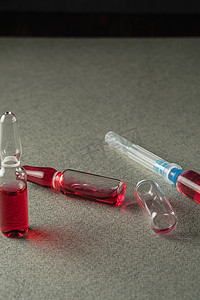 两个满的和一个空的安瓿和注射器，灰色背景上装有红色药物。