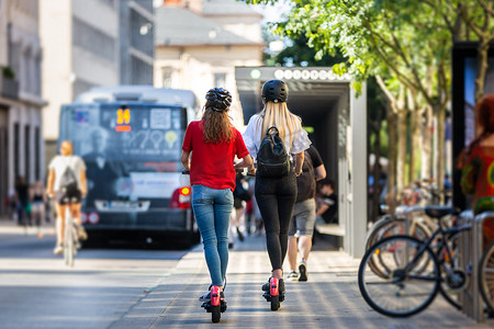 城市环境中时尚时尚少女骑公共租赁电动滑板车的后视图。