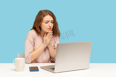 抱歉摄影照片_在蓝色背景上使用笔记本电脑的情感年轻女子。