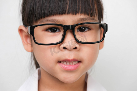 一个微笑的小女孩的肖像，戴着医生或科学服装的眼镜，背景为白色。