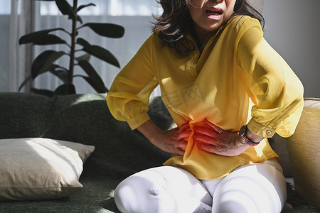 痛苦小人摄影照片_不快乐的中年女士触摸腹部，腹部疼痛，症状胃肠系统疾病，肠道，消化问题