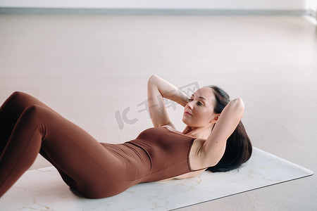 女士西装摄影照片_一位身穿棕色西装的女士在健身房里做瑜伽。