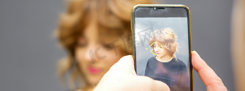 男美发师在智能手机上为客户的发型在灰色背景下拍照。