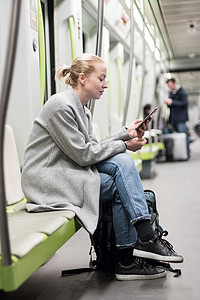 地下摄影照片_可爱的女孩在几乎空荡荡的公共地铁列车上用手机打字的肖像。
