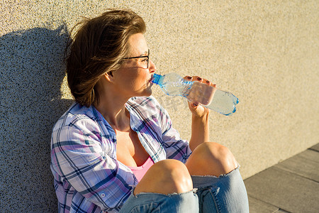 炎热的夏日，戴眼镜的成年女性正在喝瓶子里的水