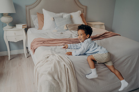 玩耍小孩子摄影照片_快乐的非洲裔美国小孩子在床上享受室内玩耍的时光