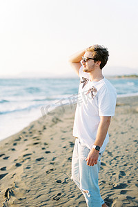 戴墨镜的男人站在海滩上，在风中拉直头发