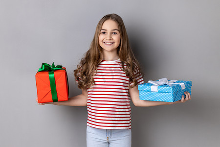 小女孩庆祝她的生日，手里拿着两个礼物盒，看着相机。