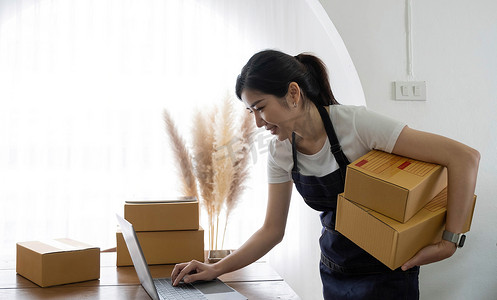 初创快乐的亚洲女企业主在家中使用盒子，准备包裹递送中小企业供应链、采购、包裹盒子递送给客户，在线中小企业企业家的想法，