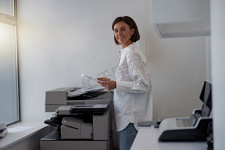 复印扫描的人摄影照片_现代办公室里微笑的女工在复印机上扫描文件