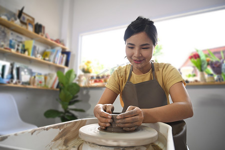 集中的亚洲年轻女性穿着围裙在陶器车间雕刻粘土菜肴