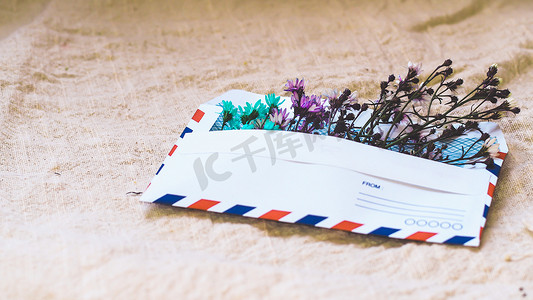 信封背景摄影照片_打开的信封，亚麻背景上有小花布置，顶视图。