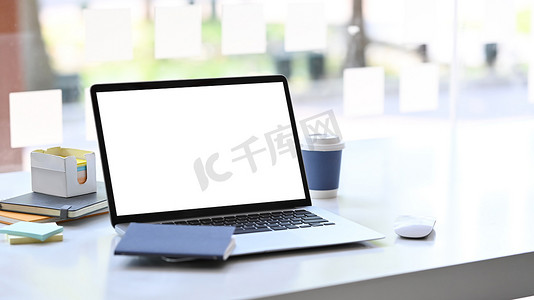 创意办公室白桌上配有空显示屏、笔记本和咖啡杯的电脑笔记本电脑。