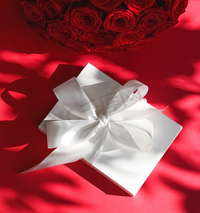 生日摄影照片_豪华假日丝绸礼盒和红色背景玫瑰花束、浪漫惊喜和鲜花作为生日或情人节礼物