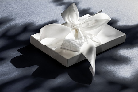 装饰礼物盒摄影照片_黑色背景上带丝带和蝴蝶结的豪华假日白色礼盒、豪华婚礼或生日礼物