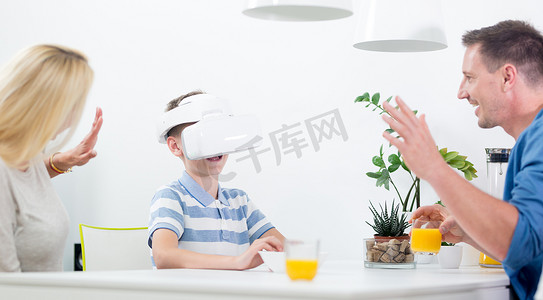 快乐的白人家庭在家里的餐桌上，用虚拟现实耳机玩游戏