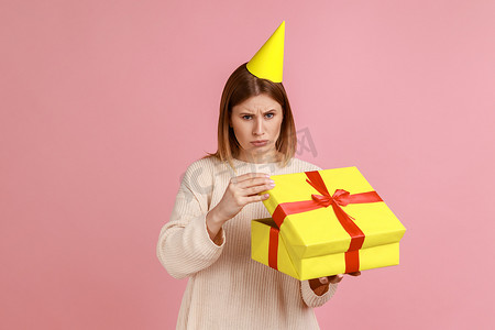 幻灭摄影照片_不快乐的金发女人在圆锥体中打开礼物盒，对礼物感到失望，看着相机。
