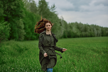 春天阴天，一位穿着长雨衣的美女跑过高草丛中的田野