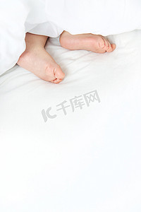 宝宝用脚睡在白色的床上。