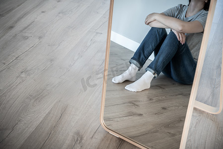 一个悲伤的女人独自坐在空荡荡的房间的地板上，绝望和孤独的概念与复制空间，灰色色调的镜子中的反射
