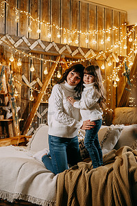沙发加背景摄影照片_一个小女孩和她的母亲在圣诞树旁边的沙发上享受舒适的家庭环境。