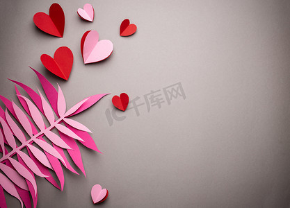 情人节折纸摄影照片_红心是从粉红色背景的纸上剪下来的，纸工艺折纸风格，从上面。