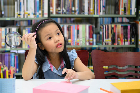 学校平面图摄影照片_亚洲女孩拿着放大镜在学校图书馆思考。