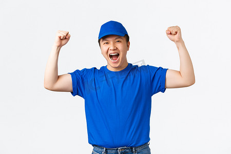 欢欣鼓舞摄影照片_兴奋而快乐、身穿蓝色制服的获胜亚洲送货员的肖像举起双手万岁的手势，欢欣鼓舞并庆祝胜利。