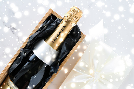 圣诞假期香槟瓶、礼盒和大理石背景上闪亮的雪