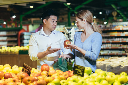 一对年轻的国际夫妇，一名女子和一名亚洲男子，正在超市挑选水果