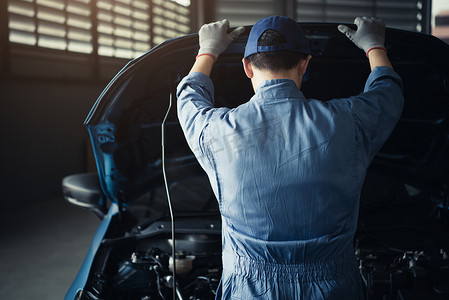 汽车修理工在汽车修理店车库根据客户索赔订单打开汽车引擎盖对维修车辆进行内部检查。