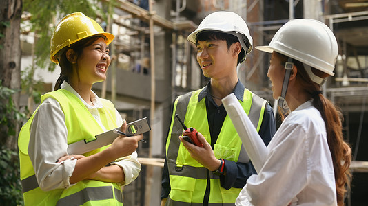 戴着安全帽和黄色背心的土木工程师团队在工业建筑施工现场规划开发细节