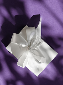 紫罗兰色背景上带丝带和蝴蝶结的豪华假日白色礼盒、豪华婚礼或生日礼物