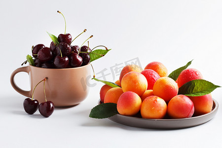 在一个杯子的樱桃和在一个板材的杏子在白色背景。