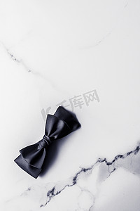 丝带邀请函摄影照片_大理石背景上的黑色丝带和蝴蝶结，平铺