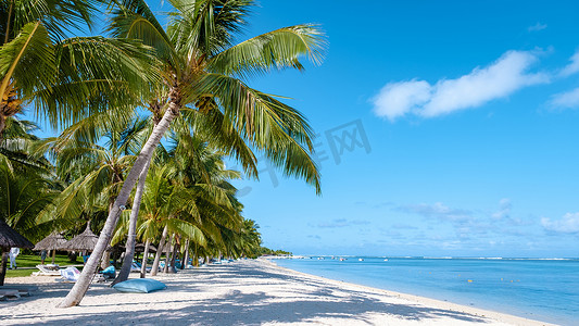 毛里求斯勒莫纳海滩的热带海滩，有棕榈树和白沙蓝色海洋，还有带伞的沙滩床、太阳椅和遮阳伞在热带海滩的棕榈树下