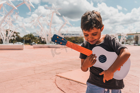 声学的摄影照片_一个拉丁裔男孩在公共广场弹奏尤克里里的喜怒无常的照片